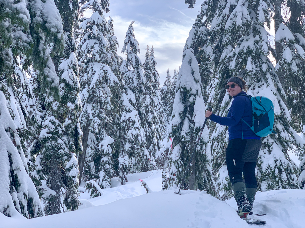 A woman wearing a down skirt snowshoes through a snowy forest