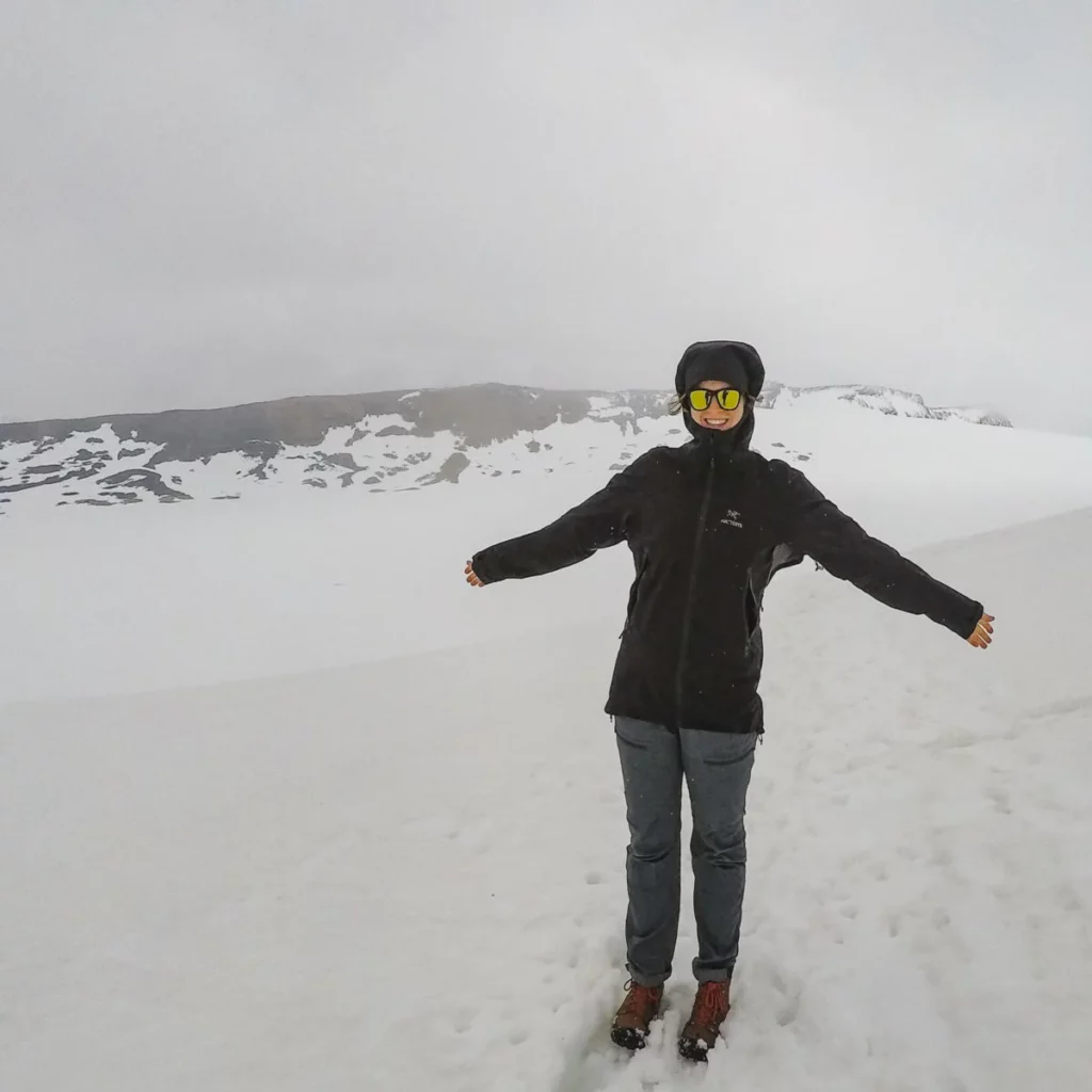 A woman wearing a black jacket and Fjallraven Abisko Lite trekking pants poses on a snowy mountain.