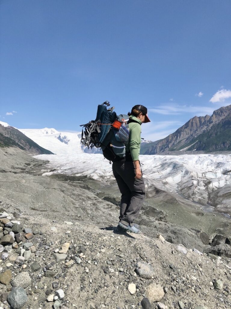 A woman wearing a backpack and REI Co-op Sahara Convertible Pants walks next to a glacier in Alaska