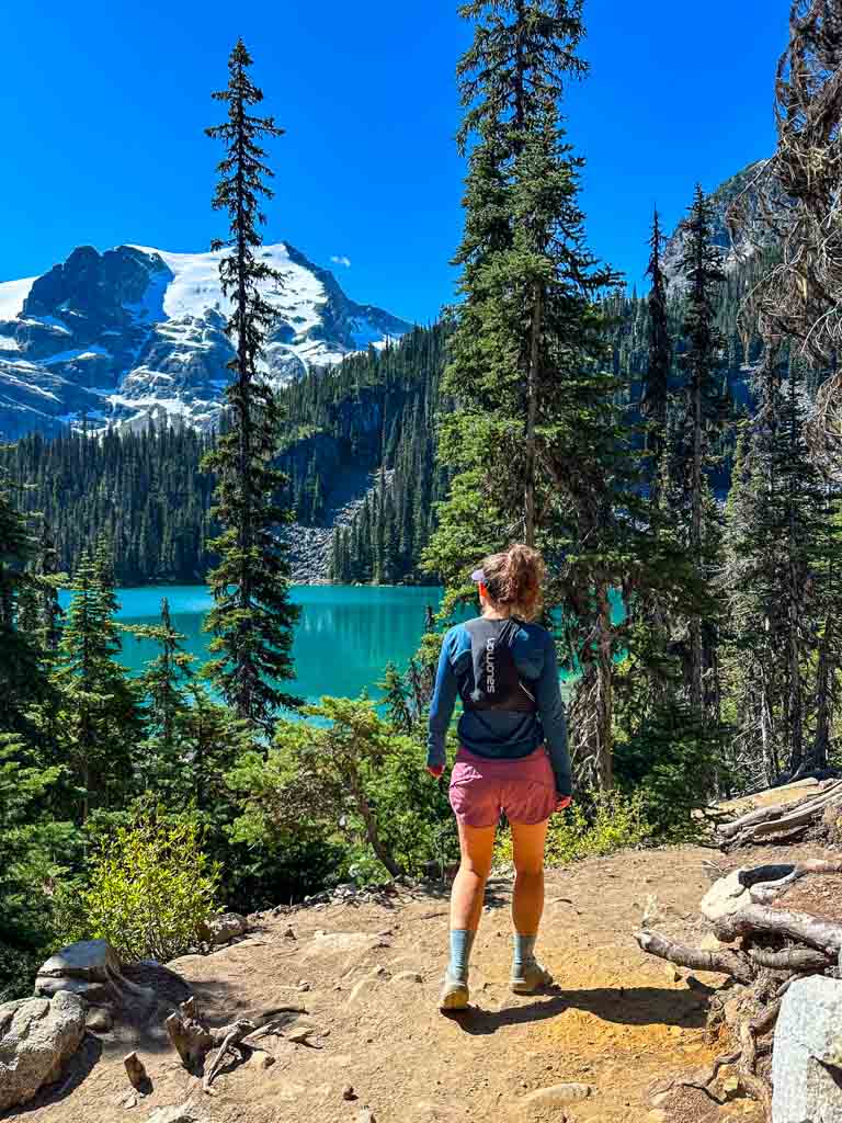 A woman hikes past a turquoise mountain lake