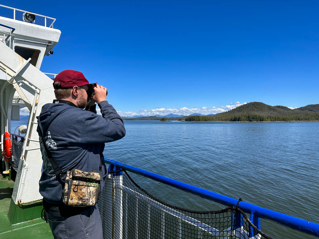 A man looks through binoculars on the ferry to Haida Gwaii