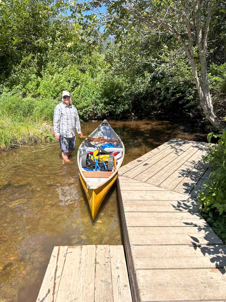 A man stands in the water next to a canoe at the dock at the Alta Lake Fish Weir