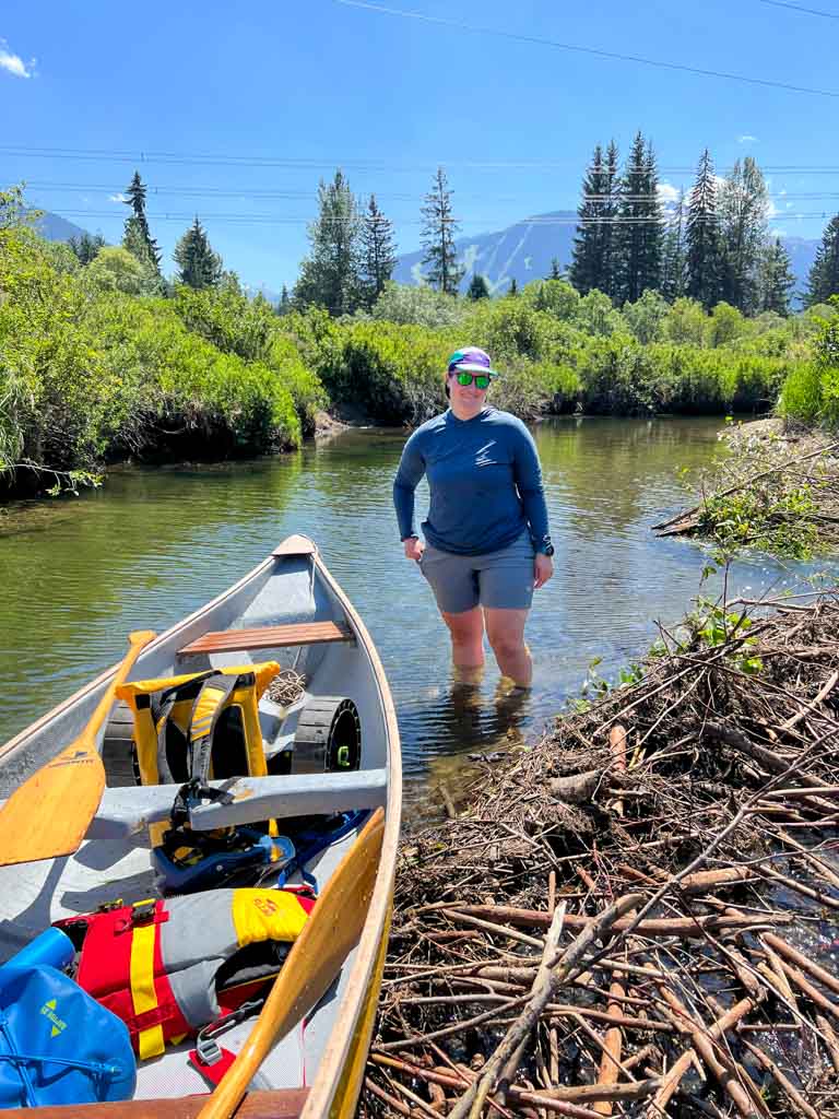 A woman pushes a canoe over a beaver dam in a river in Whistler