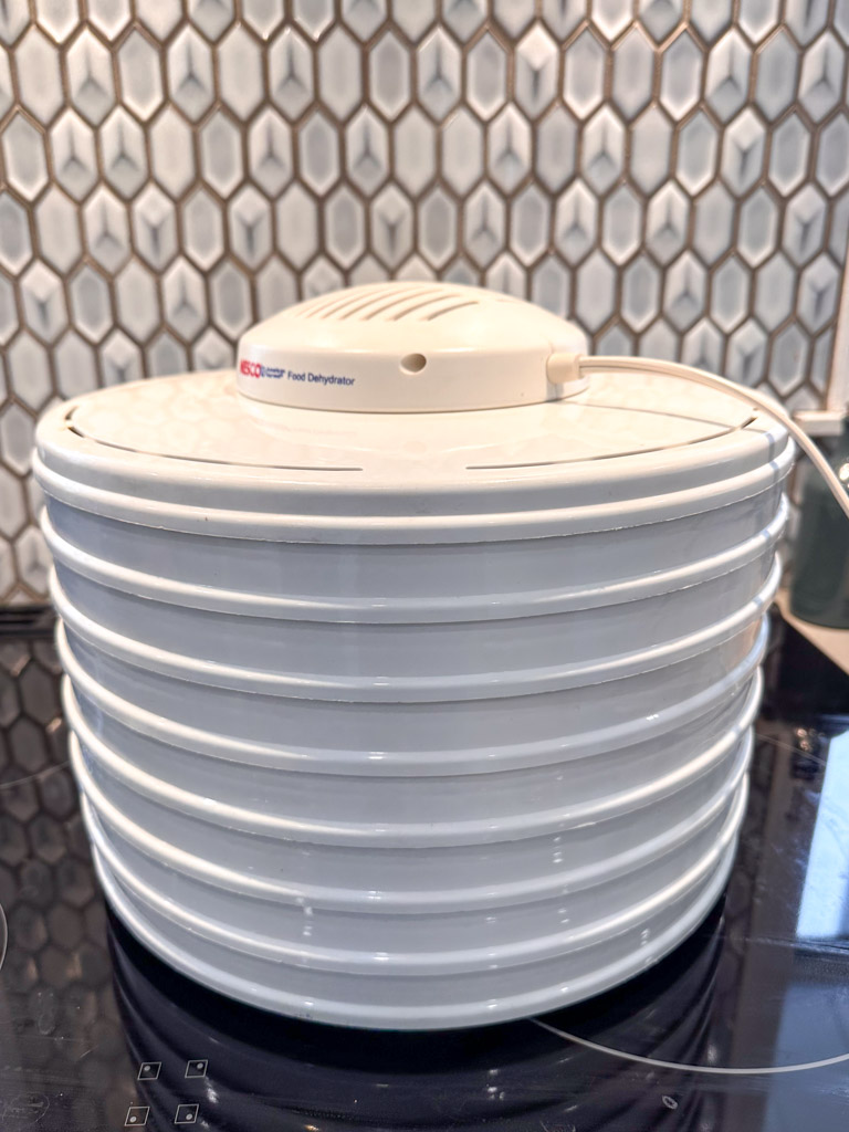 A basic Nesco dehydrator in front of a tile backsplash