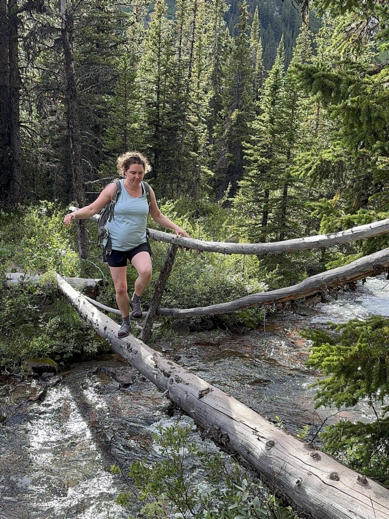 A hiker crosses a log bridge on the Merlin Lake Trail