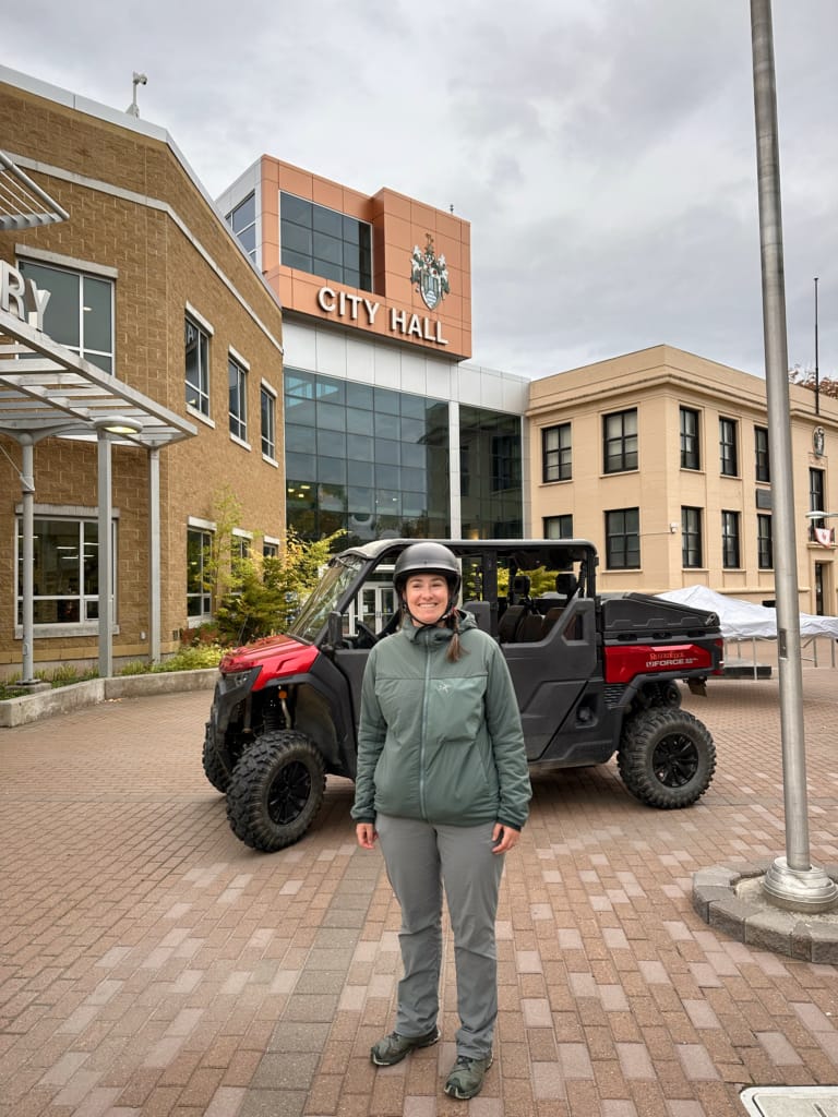 A woman poses with an ATV in front of Corner Brook City Hall