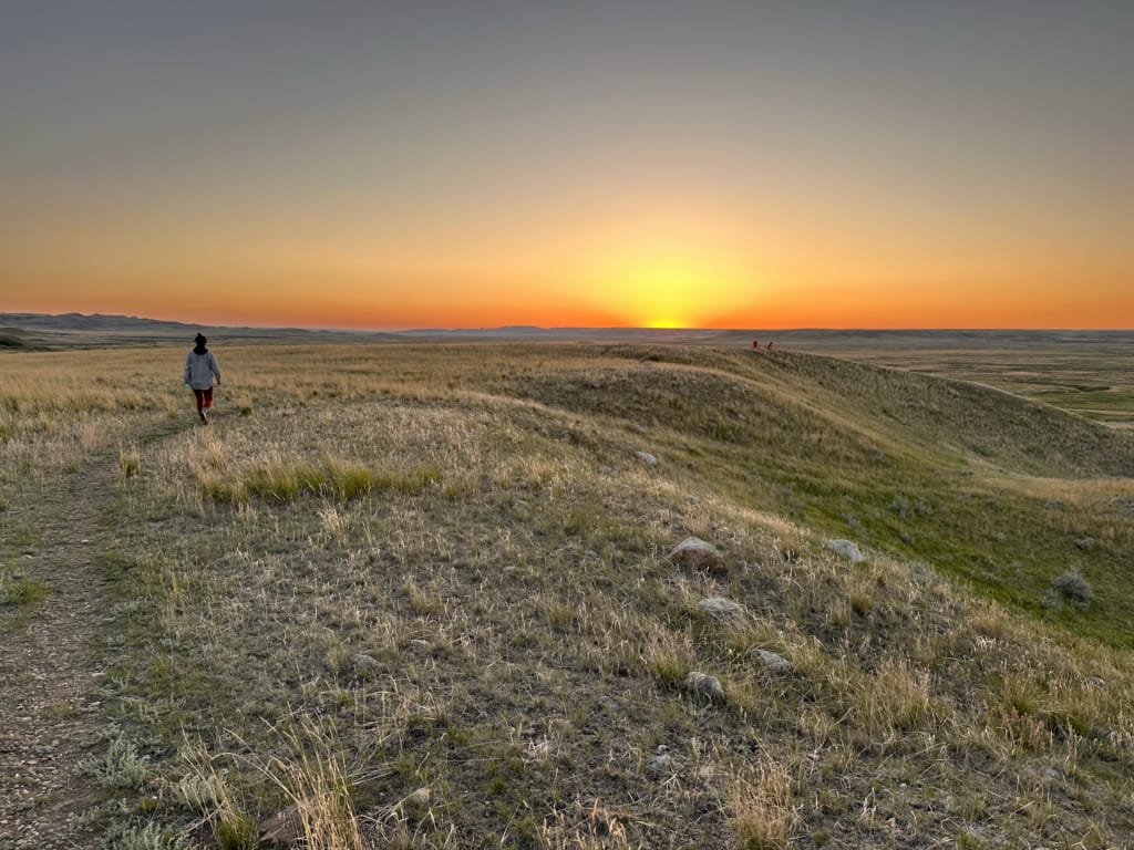A woman walking towards Parks Canada red chairs at sunset in Grasslands National Park