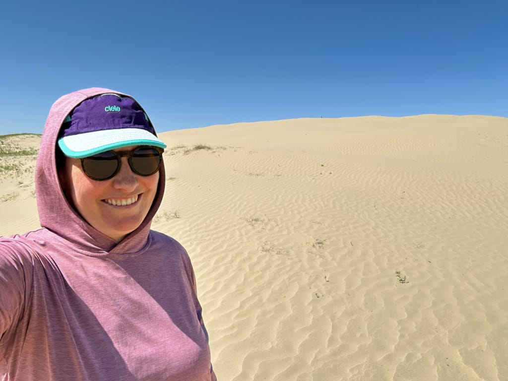 A woman wearing a sun hoodie takes a selfie at the Great Sand Hills