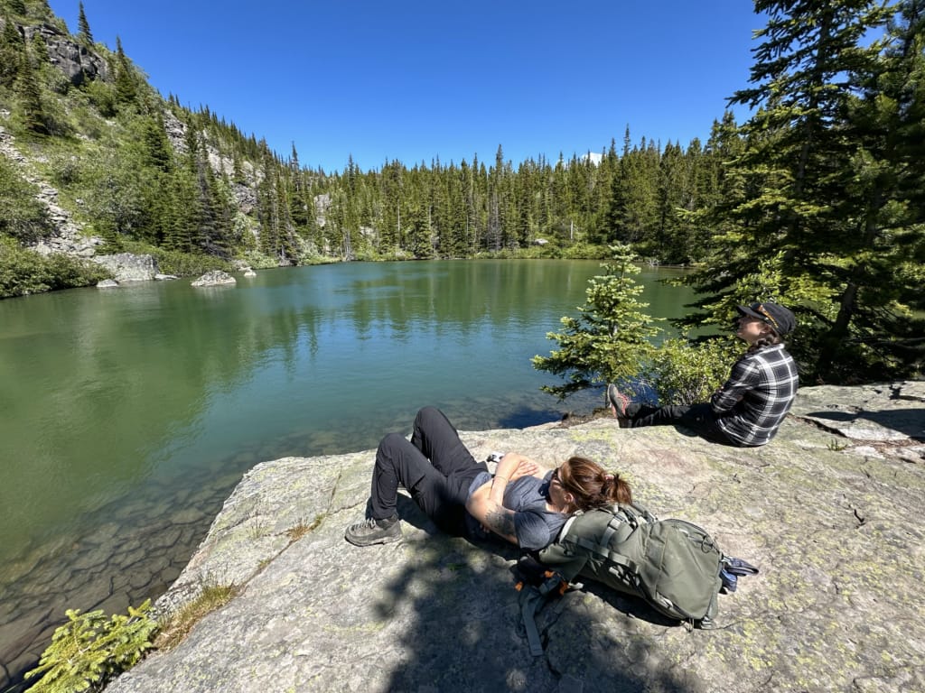 Two women lounging on a rock next to Boulder Tarn near Tumbler Ridge