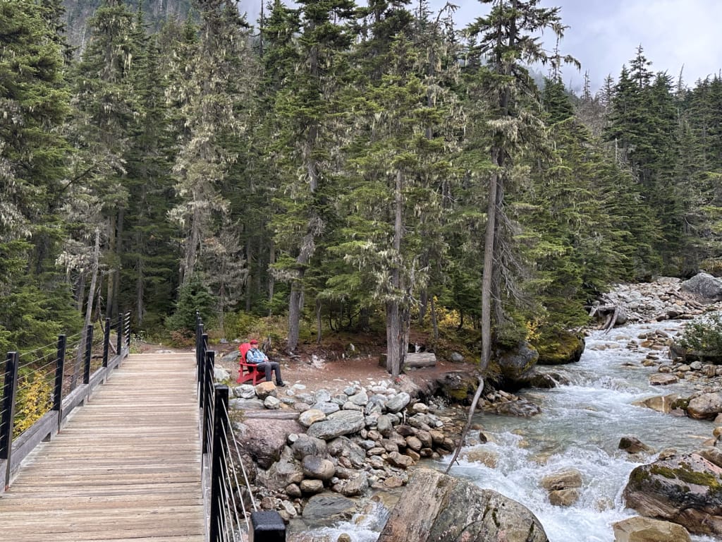 Bridge and a hiker in Parks Canada red chair on the Meeting of the Waters Trail in Glacier National Park