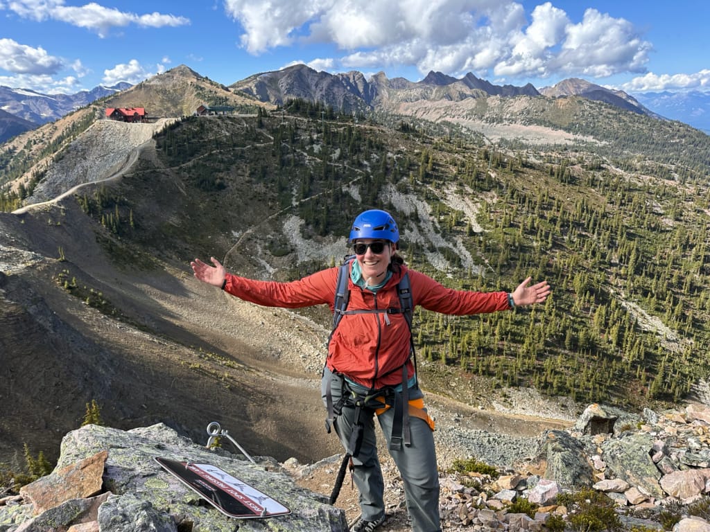 A woman poses at the top of the Kicking Horse Via Ferrata