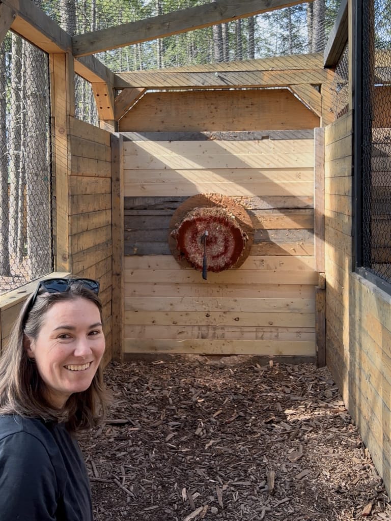 A woman smiles in front of an axe throwing bullseye