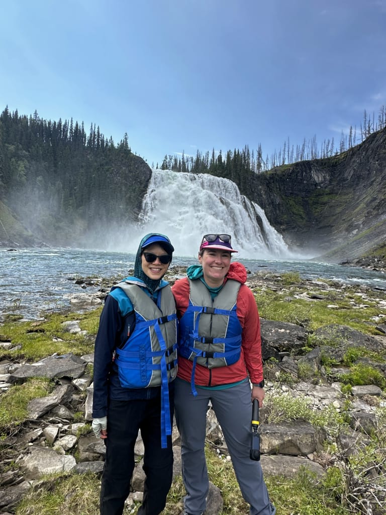 Two women wearing life jackets pose in front of Kinuseo Falls